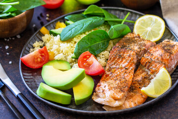 Grilled salmon fillet close-up with couscous, salad fresh vegetables and avocado on dark background.