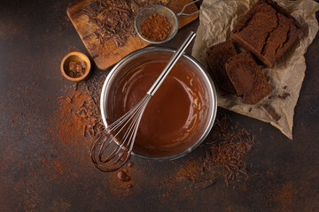 Homemade delicious chocolate vegan cake and sauce in bowl with whisk on dark wooden background