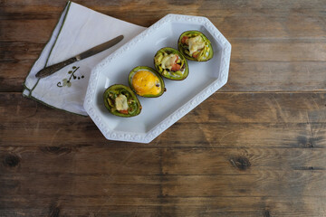 baked avocado stuffed with egg, vegetables, lie on a white dish, linen napkin with embroidery,...