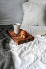 Frühstück im Bett mit einer Tasse Kaffee und einem Croissant. Schlafzimmer, Hygge, Zuhause.