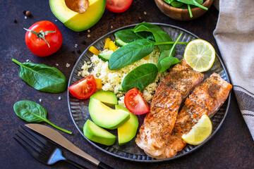 Grilled salmon fillet close-up with couscous, salad fresh vegetables and avocado on dark background.