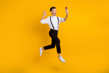 Fototapeta na wymiar Full length body size photo of jumping man taking selfie waving hand video call isolated on vibrant yellow color background