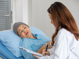 Young and beautiful doctor asking and note for diagnosis with Older Asian woman patient covered the head with clothes effect from chemo treatment in cancer cure process