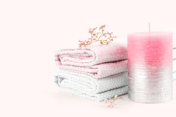 Obraz na płótnie Canvas Soft pastel spa composition. Textured decorative aroma candle, bath towels and branches of delicate wildflowers on a pale pink background. Soft focus. Copy space.