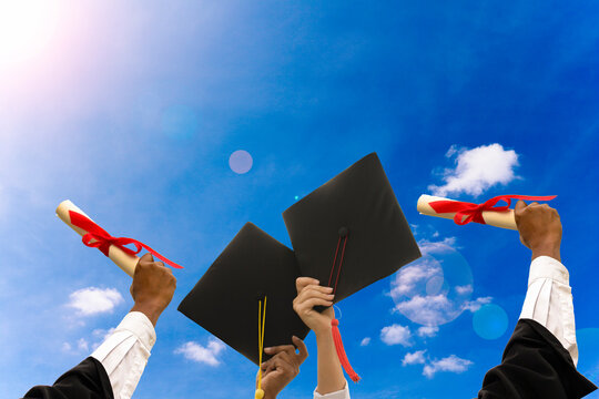 Low Angle View Of Students Holding Certificates And Mortarboards Against Sky