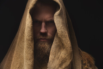 Portrait of a medieval bearded war monk dressed in animal skins and sacking. Low key. Focus on...
