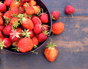 Still life with lot of ripe appetizing strawberries collected in the round bowl on vintage wooden table as background top view closeup