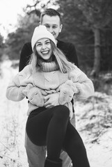 
A man circles a woman in his arms against the background of a snowy forest black and white photo