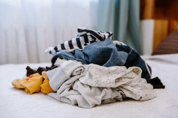 Pile of unfolded dirty clothes for laundry on the bed. Heap of used clothes for donation and recycling. Concept of minimalism, mess and wardrobe cleaning - obrazy, fototapety, plakaty