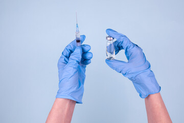 Vaccination against the new SARS-CoV-2 coronavirus. A doctor wearing blue gloves holds a bottle of coronavirus vaccine and a syringe on a blue background.