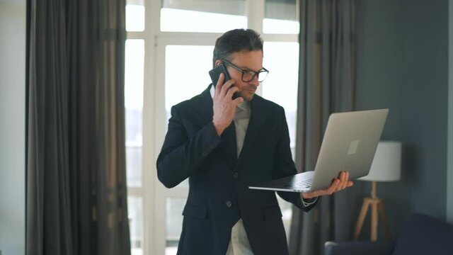 Caucasian man dressed in a jacket and underwear negotiates using smartphone and laptop at home in a modern apartment. Remote work during a pandemic