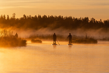 Obraz na płótnie Canvas Amazing view of two asian girls doing SUP stand up paddle boarding at sunrise in lake. Early summer morning activity