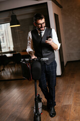 Young businessman in a suit with electric scooter. Handsome man using the phone in office.