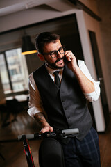 Young businessman in a suit with electric scooter. Handsome man using the phone in office.