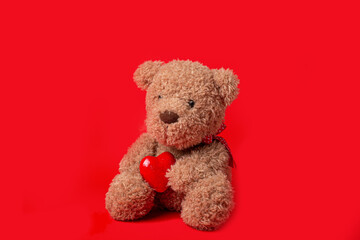 Teddy bear holding a heart on a red background