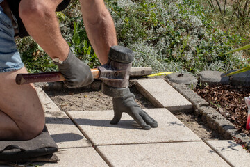 A professional paver worker laying patio slabs in a gravel bed using a professional paving hammer....