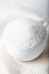 White granulated sugar in a white cup on a pile of sugar