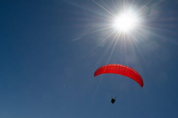 paraglider taking off in deep blue sky, flying high against the light