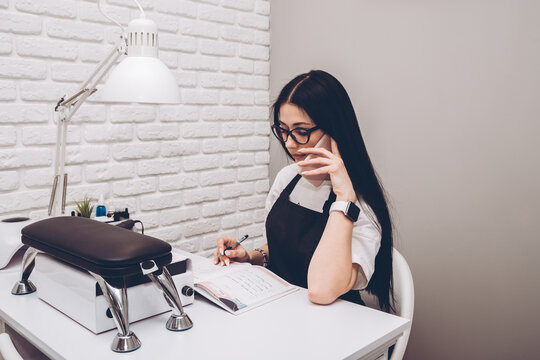 Businesswoman, conducts an appointment for a manicure procedure in a beauty salon. Business lady takes a call from clients. A manicurist in black uniform sits at his desk and speaks on the phone.