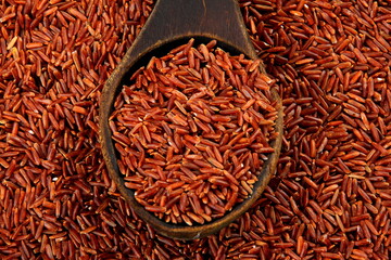 Raw red rice in a old wooden spoon on red rice background. Brown rice in wooden spoon