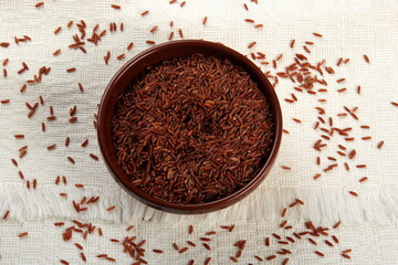 raw red rice in a clay bowl on a light fabric background. uncooked brown wild rice, top view 