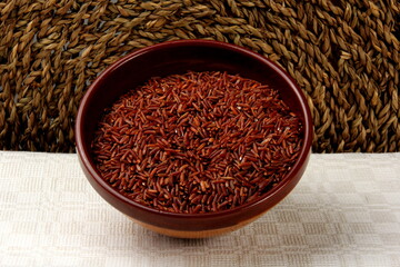 raw red rice in a clay bowl on a light fabric background. uncooked brown wild rice, top view 