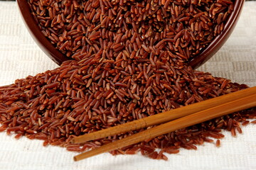 Wooden chopsticks and raw red rice in a clay bowl on a light fabric background. uncooked brown wild rice, top view 