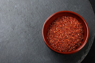 raw red rice in a clay bowl on a black stone plate. uncooked brown wild rice, top view