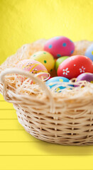easter, holidays, tradition and object concept - close up of colored eggs in basket over yellow wooden boards background