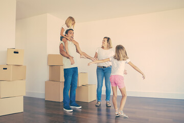 Sweet girls and their mom showing new flat to excited dad. Younger daughter riding on fathers neck. Apartment buying concept