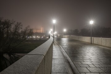 Blick über die verschneite steinerne Brücke in Regensburg nachts im Nebel über den Fluss Donau mit dem beleuchteten Dom im Hintergrund, Deutschland 2020
