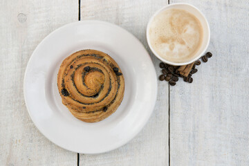 Bun on a plate and a cup of coffee on a white wooden table 