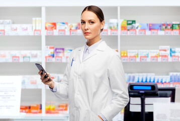 medicine, profession and healthcare concept - female doctor with stethoscope using smartphone over pharmacy background