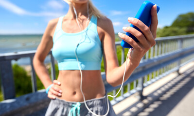 sport, fitness and technology concept - close up of happy smiling sporty young woman with smartphone and earphones