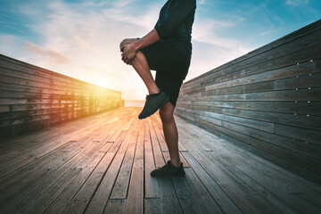 Sporty man warming up and stretching legs before workout outdoors at sunset or sunrise. Stretching...