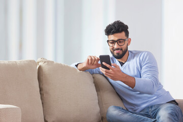 Young man sitting on the couch and using his mobile. 	