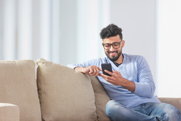 Young man sitting on the couch and using his mobile. 	