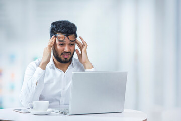 Young man holding his head in frustration due to workload in office. 