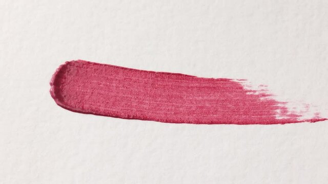 pink cosmetic lip gloss smear example is applied on a white background with an applicator brush close up