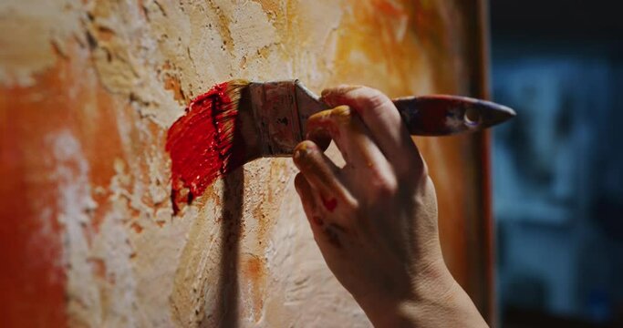 Cinematic macro shot of female creative artist painter concentrated and inspired painting abstract picture with paint brush and oil colors on canvas while working on new masterpiece for exhibition.