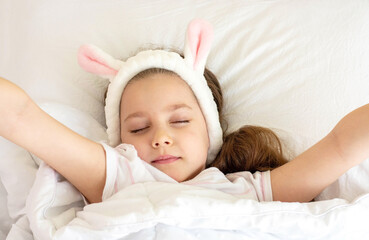 A little girl is sleeping in a bed under a white blanket, with rabbit ears. I wake up early in the morning. The concept of celebrating Easter.
