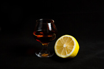 a glass of cognac with half a lemon on a black background