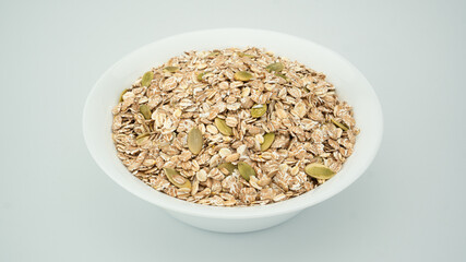 Golden oatmeal mixed with peeled pumpkin seeds in a round white bowl