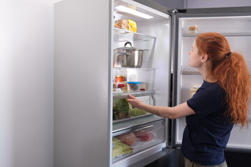 Fototapeta na wymiar Woman standing at the open refrigerator with fruits, vegetables and healthy food