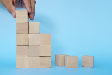 Hand putting together broken or fallen building blocks in blue background. Economic recovery,...