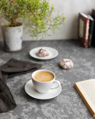 White cup of coffee, red velvet biscuits, houseplant and open book on a dark gray concrete background. Selective focuse.