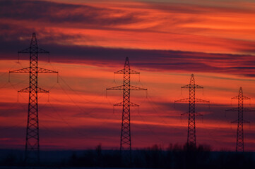 Fototapeta premium High voltage poles photographed at a beautiful sunset. Red background.