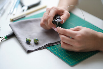 Woman using pliers to adjust malachite gemstones. Craft jewelery making with professional tools. A...