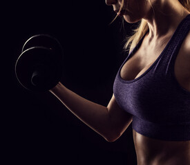 Slim athletic woman Holding dumbbell in the hand on black