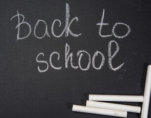 lettering back to school in white chalk on a black school board and a piece of chalk